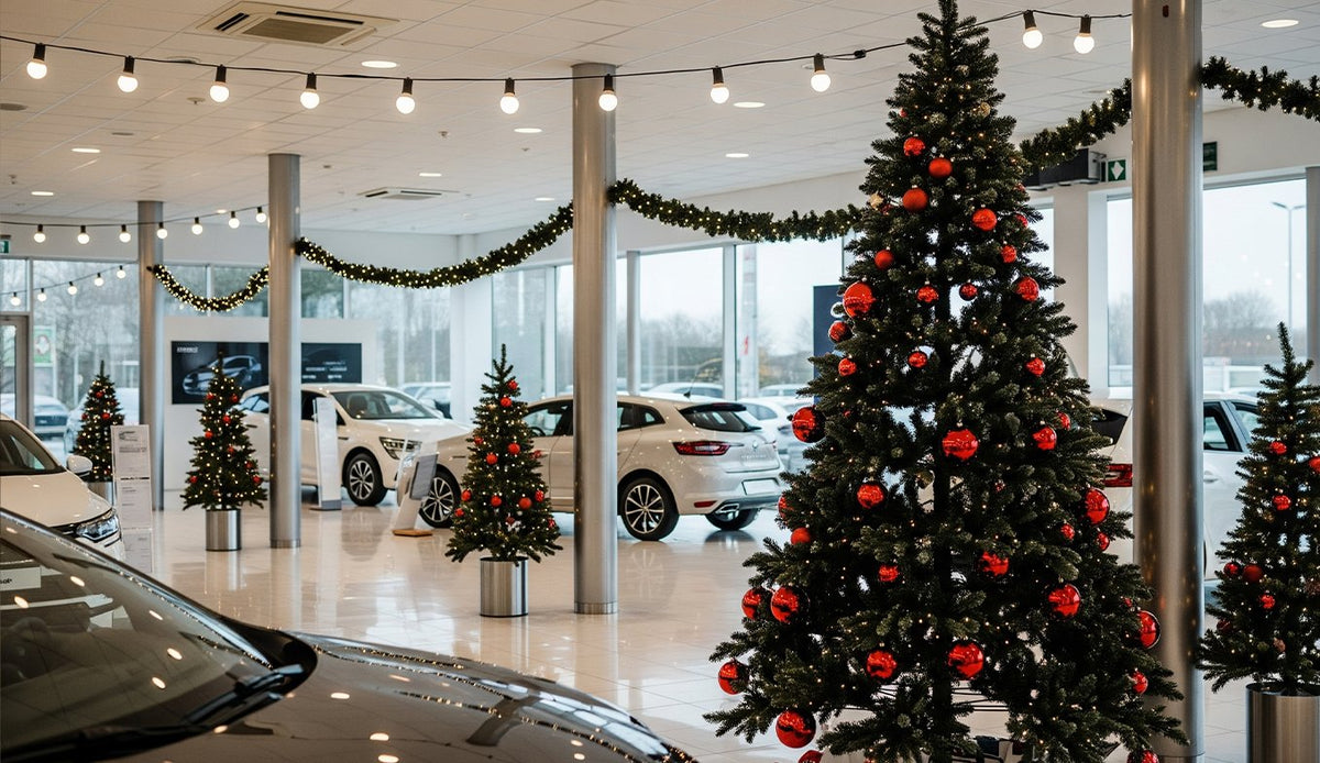 Sapins à boules rouges et guirlandes d'ampoules dans un showroom automobile, entre les voitures